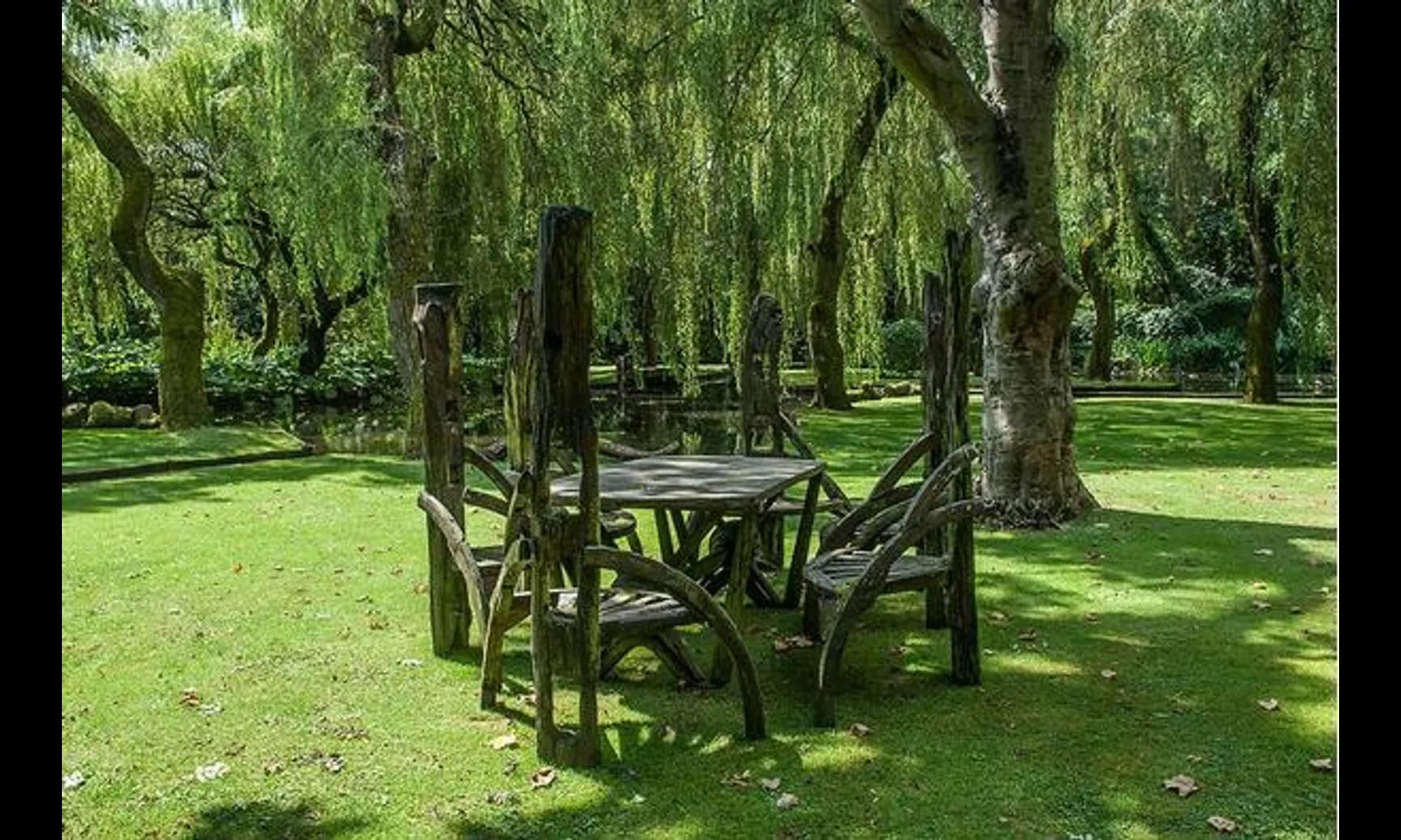 A rustic timber table and chairs set under willows on the lawn at Netley Mill House